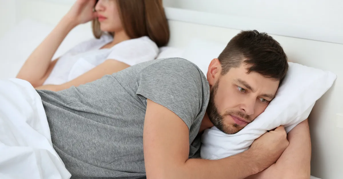 Smutny mężczyzna leży w łóżku z kobietą - nawiązanie do dysfunkcji seksualnych